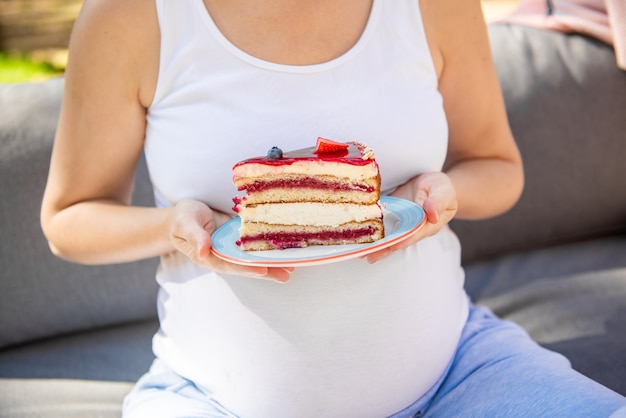 Happy pregnant woman eating sweet cake in summer Park