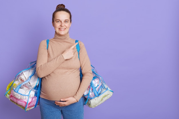 母性の家に赤ちゃんと自分のための服とバッグを保持している幸せな妊婦