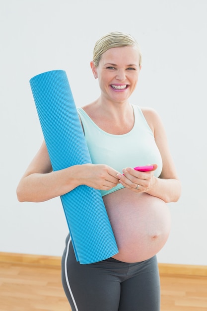 Happy pregnant woman holding exercise mat sending a text message