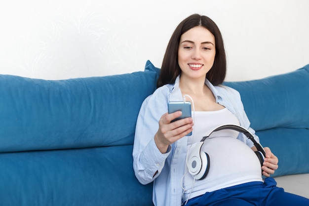 happy pregnant woman holding headphones on her belly at home Pregnancy people technology concept