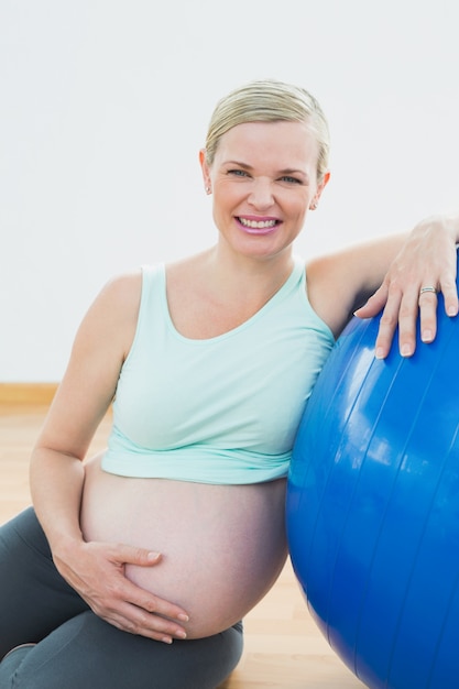 Happy pregnant woman leaning against exercise ball holding her belly