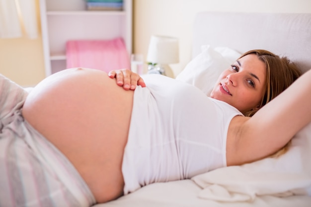 Happy pregnant woman lying on bed 