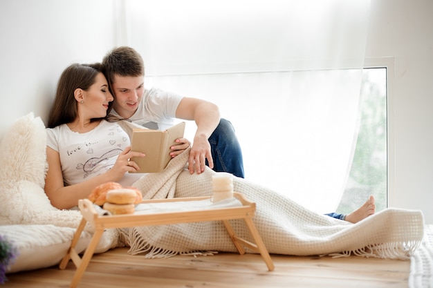 Happy pregnant woman lying and reading book on the bed with husband