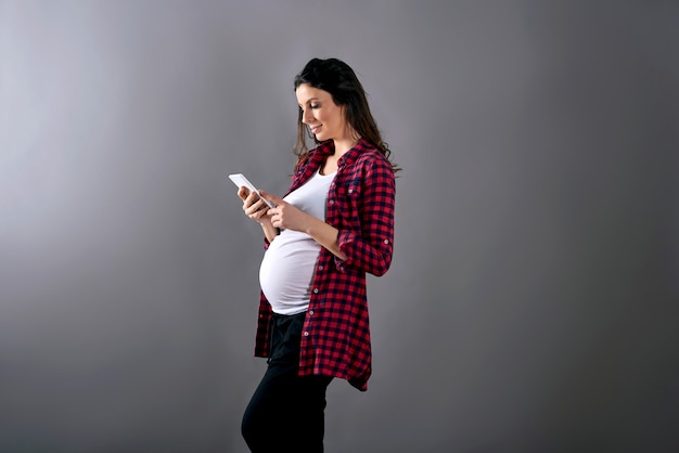 A happy pregnant woman in a red shirt using a smartphone