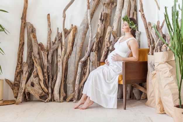 Happy pregnant woman sitting on armchair and touching her belly