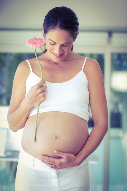 Happy pregnant woman standing with flower at home