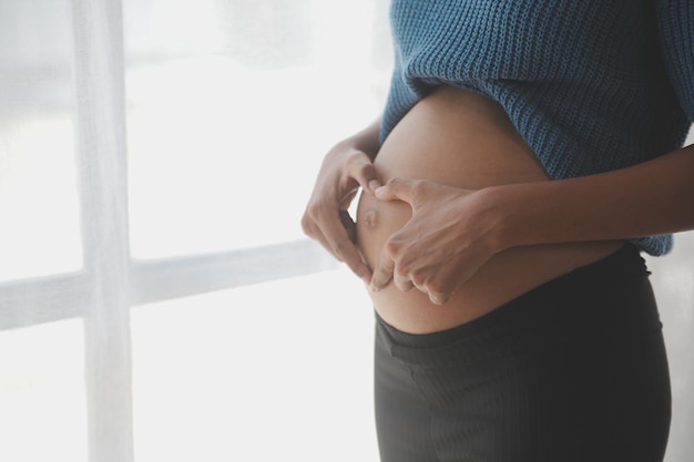 Счастливая беременная женщина трогает живот перед белой стеной