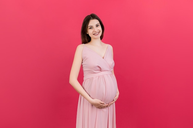 Happy pregnant woman touching her abdomen at Colored background Future mother is wearing white underwear Expecting of a baby Copy space