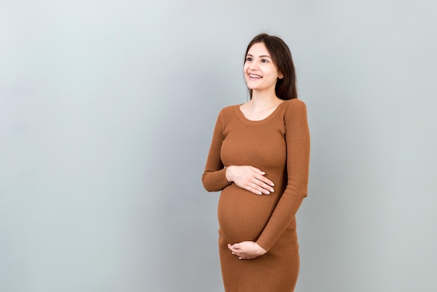 Happy pregnant woman touching her abdomen at Colored background Future mother is wearing white underwear Expecting of a baby Copy space