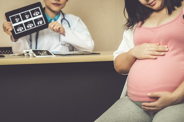 행복 한 임신 한 여자는 임신 컨설턴트를 위해 병원이나 클리닉에서 산부인과 의사를 방문합니다.