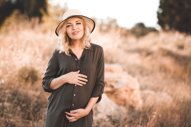 Happy pregnant woman wearing stylish dress and hat