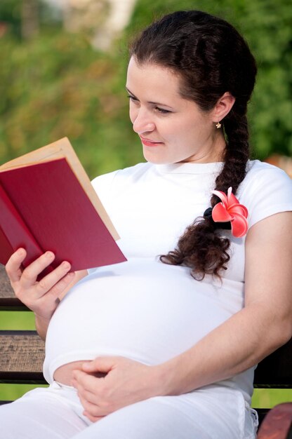 Happy pregnant woman with book in park outdoors