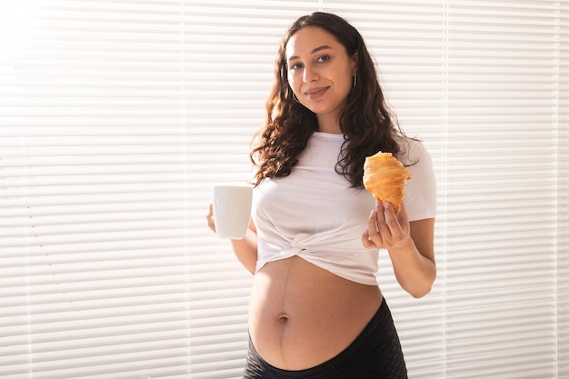 Happy pregnant woman with croissant buns at home pregnancy eating and people concept