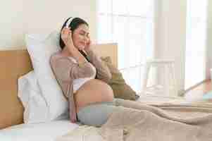 Photo happy pregnant woman with headphones listening to mozart music and lying on bed pregnancy concept