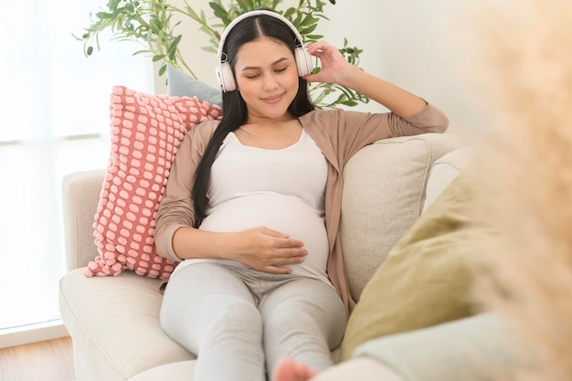 Happy pregnant woman with headphones listening to mozart music and lying on sofa pregnancy concept