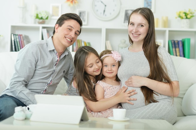 Счастливая беременная женщина с мужем и дочерьми сидят дома на диване
