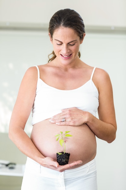 Happy pregnant woman with new plant in palm standing at home