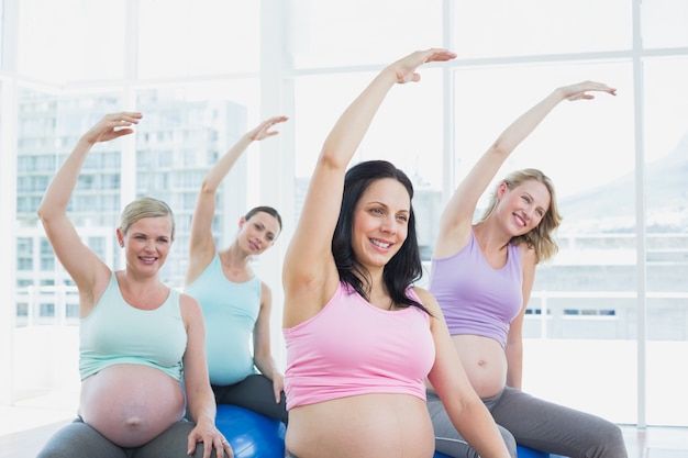 Happy pregnant women sitting on exercise balls stretching arms