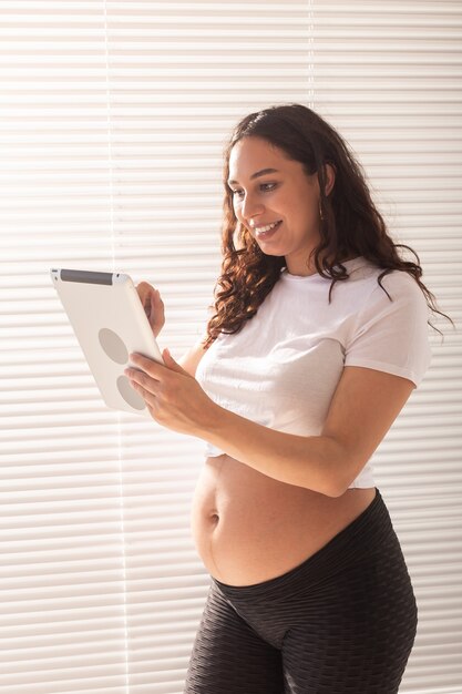 ビデオ接続とタブレットを使用して彼女の夫と話している幸せな妊娠中の若い美しい女性