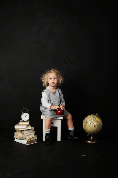 Ragazza prescolare felice con libri, un globo e un orologio su un fondo nero