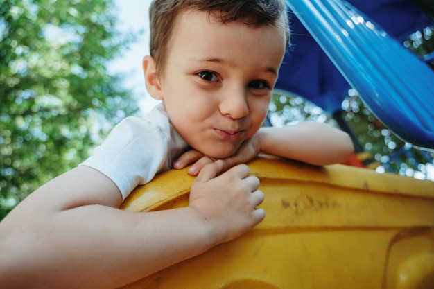 happy preschooler boy playing on a slide on the playground in summer