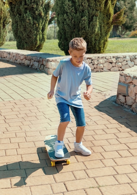 Happy preschooler boy in shirt learning to ride a skateboard