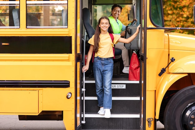 Photo happy preteen girl getting of the yellow school bus smiling at camera