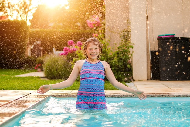 写真 雨水の下でプールで楽しんで幸せなプレティーンの女の子は夕暮れ時の庭で屋外でドロップします。