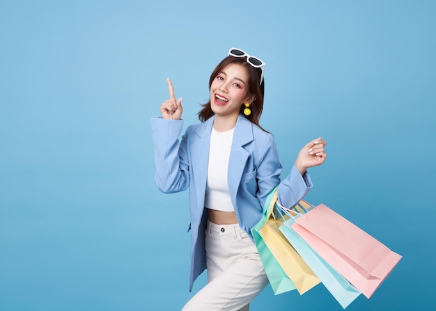 다채로운 쇼핑 가방을 들고 있는 행복하고 예쁜 아시아 여성이 손가락을 가리키고