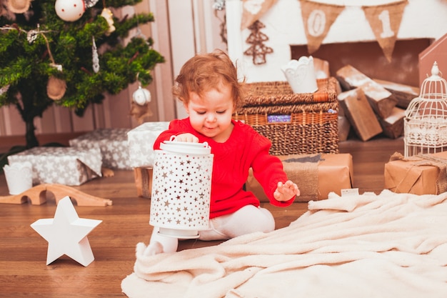 Happy pretty baby dressed in red dress with Christmas gifts