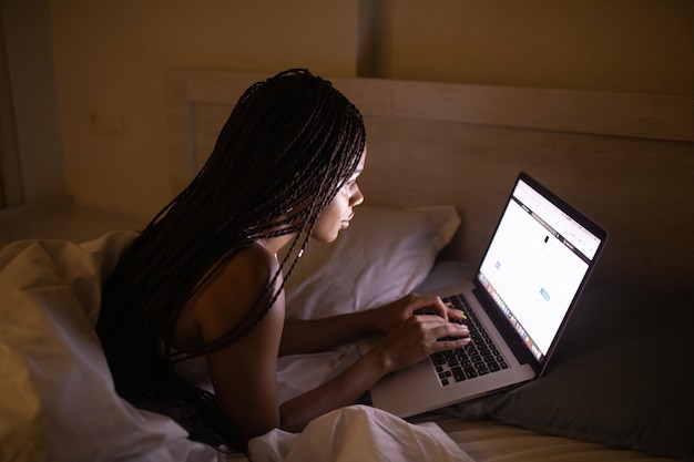 Happy pretty black woman using laptop on bed. Woman using laptop at night.