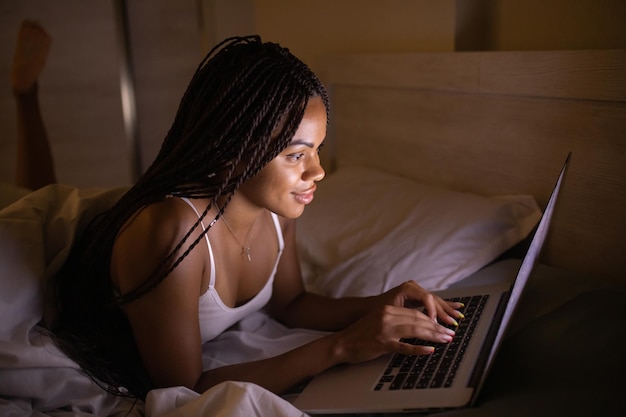 Happy pretty black woman using laptop on bed. Woman using laptop at night.