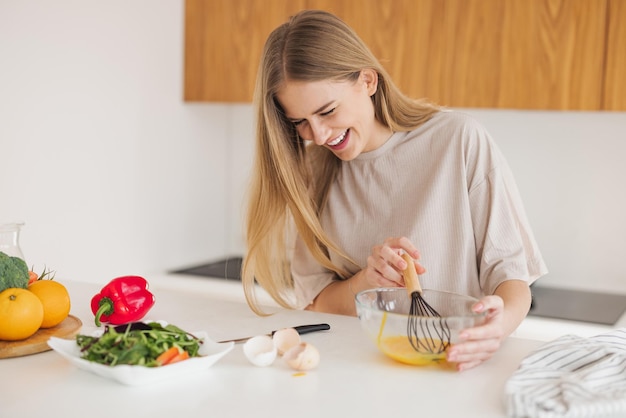 パジャマを着た幸せなかなり金髪の女性が、自宅のキッチンで朝食に卵を叩いている