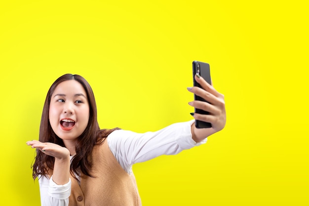 Felice bella ragazza fa autoritratto sullo smartphone su sfondo giallo.