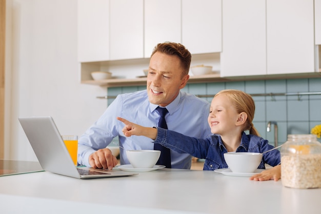 Happy pretty nice girl sitting together with her father and pointing at the laptop screen