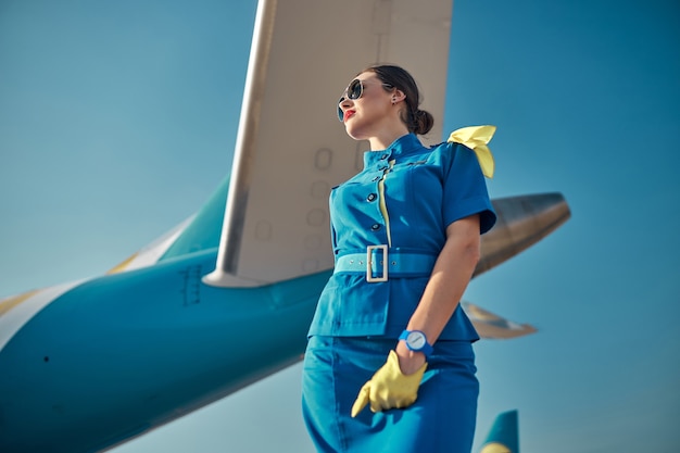 Happy pretty stewardess near passenger plane outdoors