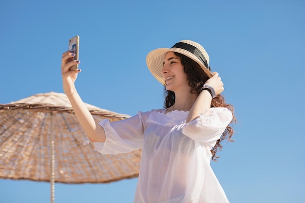 ソーシャルメディアのためにselfieショットを撮ってカメラを見て幸せなかわいい十代の少女晴れた日に麦わら帽子で笑顔のティーンエイジャーのヘッドショットの肖像画