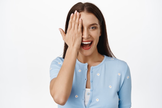 Felice bella donna sulla trentina, con metà del viso, un occhio con il palmo della mano, sorridente e ridente