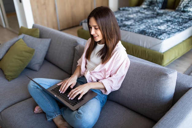 Happy pretty woman using laptop sitting on cosy sofa