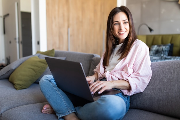 Happy pretty woman using laptop sitting on cosy sofa