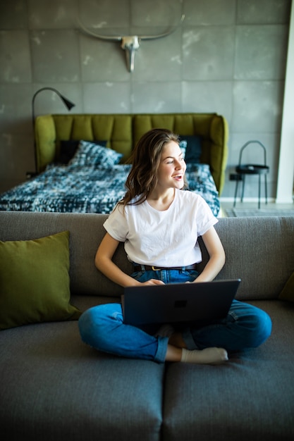 Happy pretty woman using laptop sitting on cosy sofa