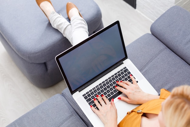 Happy pretty woman using laptop sitting on cosy sofa