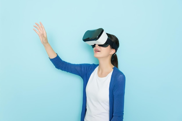 VRデバイスのヘッドセット機器を身に着け、青色の背景でオンラインショッピングのウェブサイトを閲覧し、商品を探すジェスチャーをする幸せなきれいな女性。