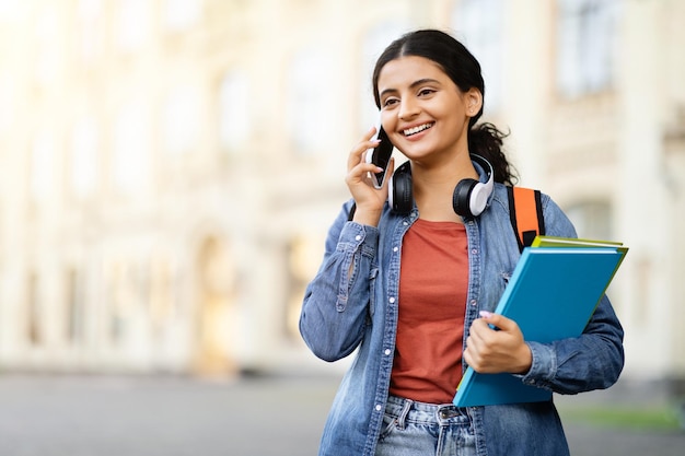 Happy pretty young indian woman student talking on phone outdoor