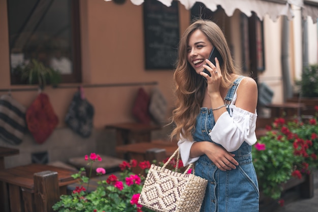 Happy pretty young teenager girl holding bags keeping a conversation with the mobile phone