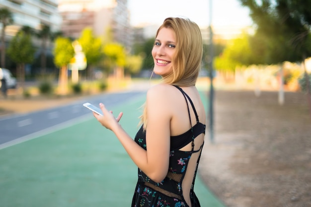 Happy pretty young teenager girl in a park sending a message or email with the mobile