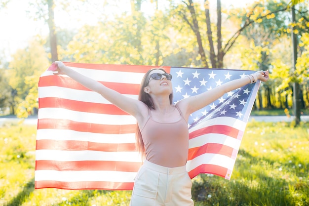 幸せなかなり若い女性は旗を保持します米国の愛国的な休日とお祝いの独立記念日4日