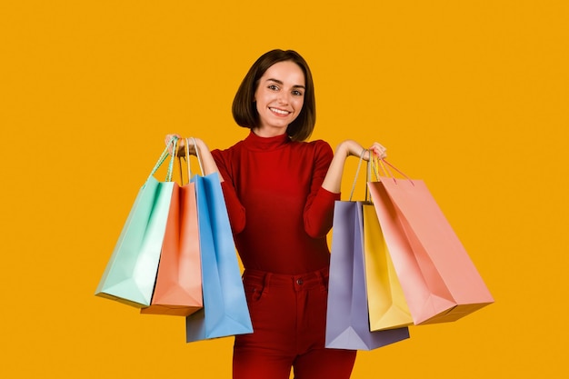 Happy pretty young woman holding colorful shopping bags on orange