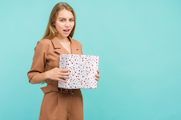 Happy pretty young woman holding gift box over blue background