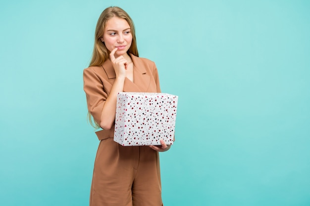 Happy pretty young woman holding gift box over blue background.